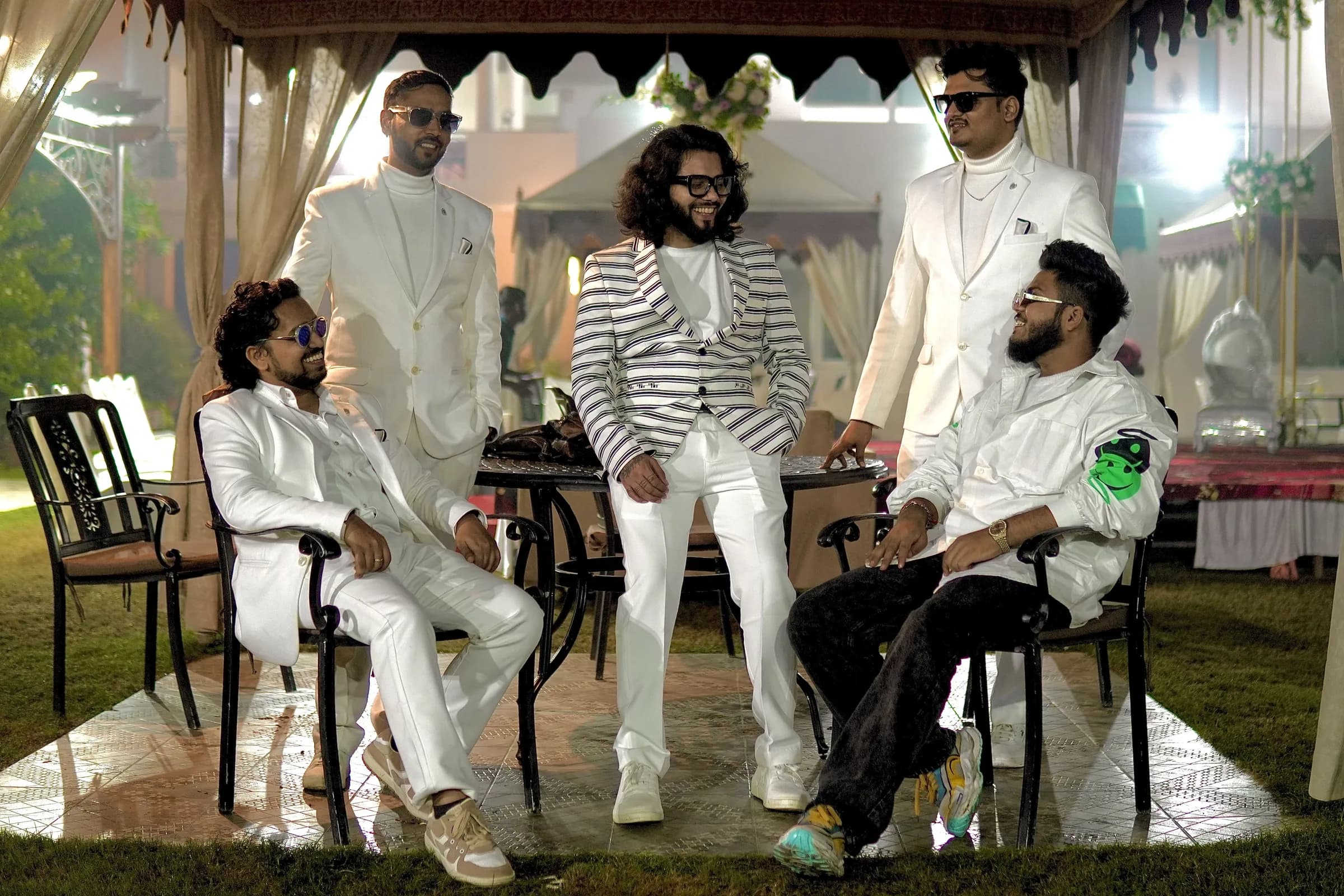 The five members of Softrock in white suits, posing together around a table in an outdoor garden venue.