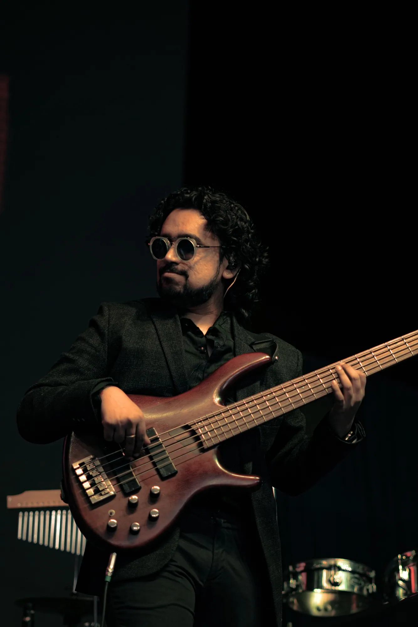 Softrock's bassist in sunglasses playing a five-string bass on a dark stage.