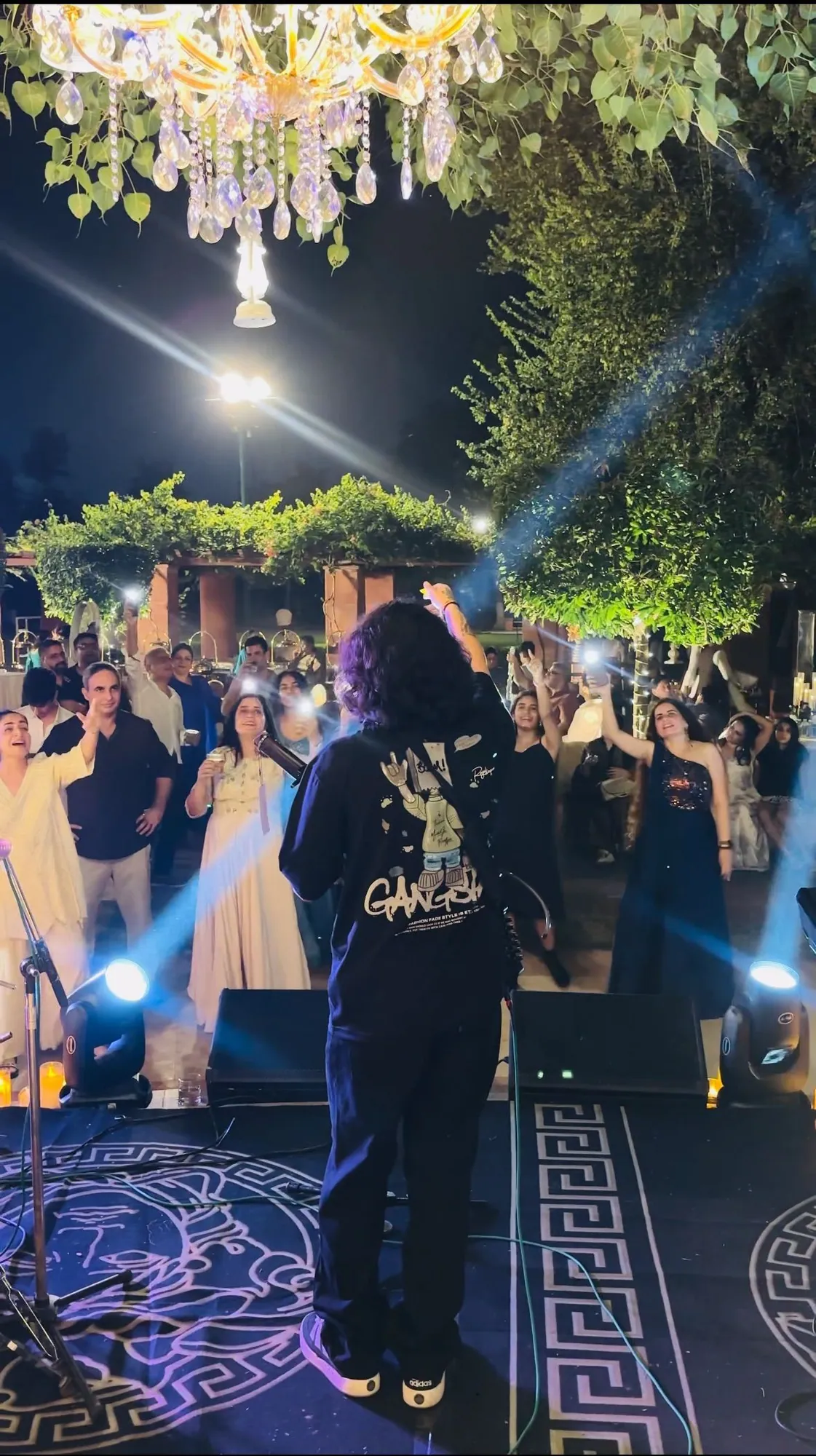 Softrock's vocalist seen from behind, facing guests dancing with their arms up beneath a crystal chandelier.