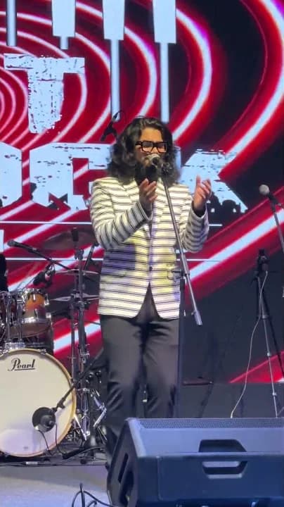 Softrock's vocalist in a striped blazer singing in front of the Softrock logo screen.
