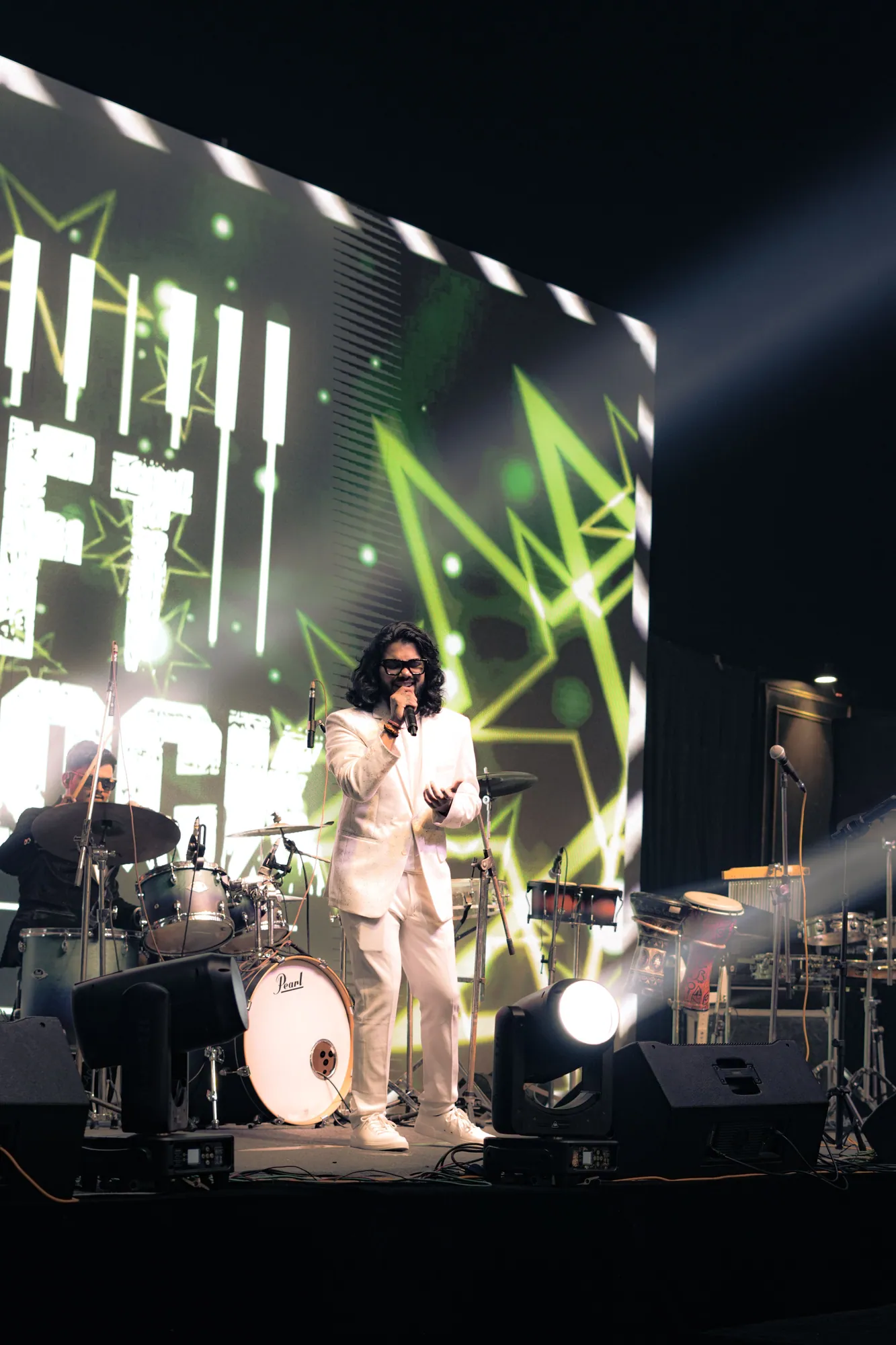 Softrock's vocalist in a white suit on a large stage, a giant LED screen and drum kit behind and a light beam cutting across.