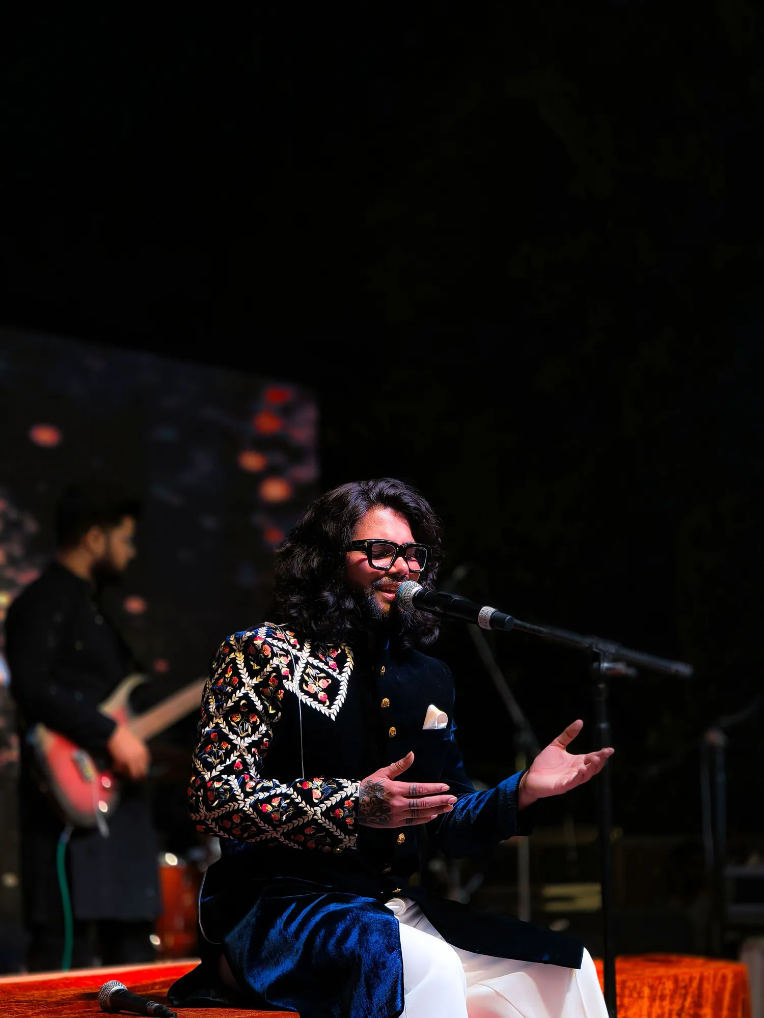 Softrock's vocalist seated mid-song, arms open, with a guitarist playing behind.