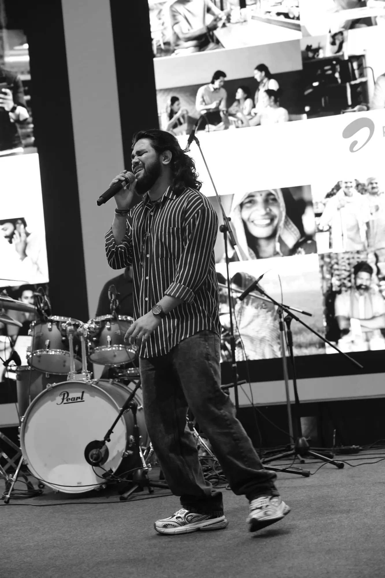Black-and-white shot of Softrock's vocalist singing mid-stride in front of the drum kit and a photo-collage screen.
