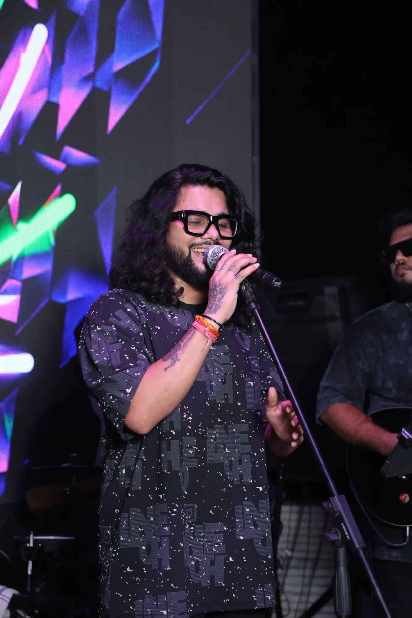 Softrock's vocalist in a sequinned shirt singing at the microphone under neon stage visuals.