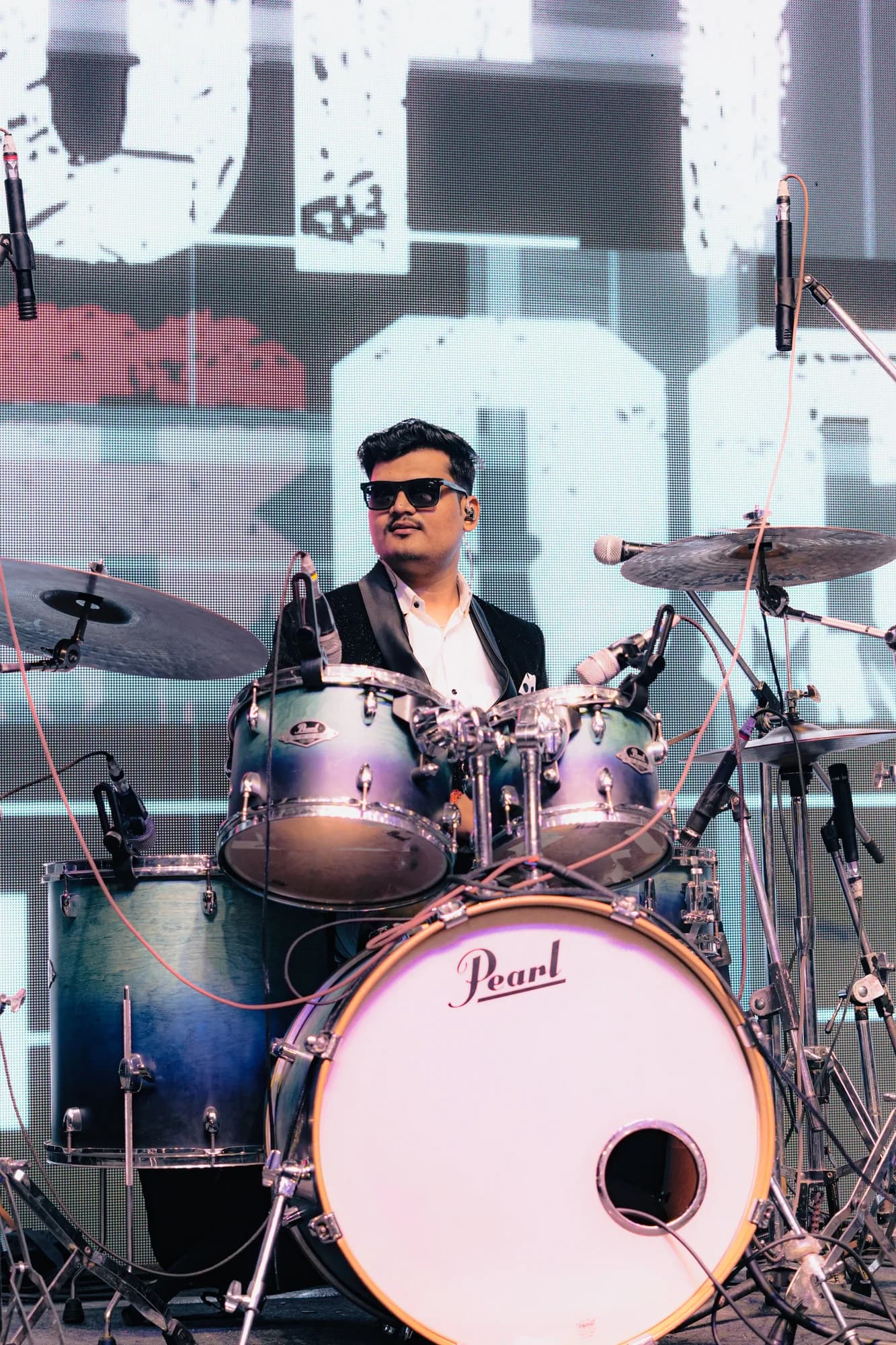 Softrock's drummer in a suit and sunglasses behind a Pearl kit, the Softrock logo screen behind.