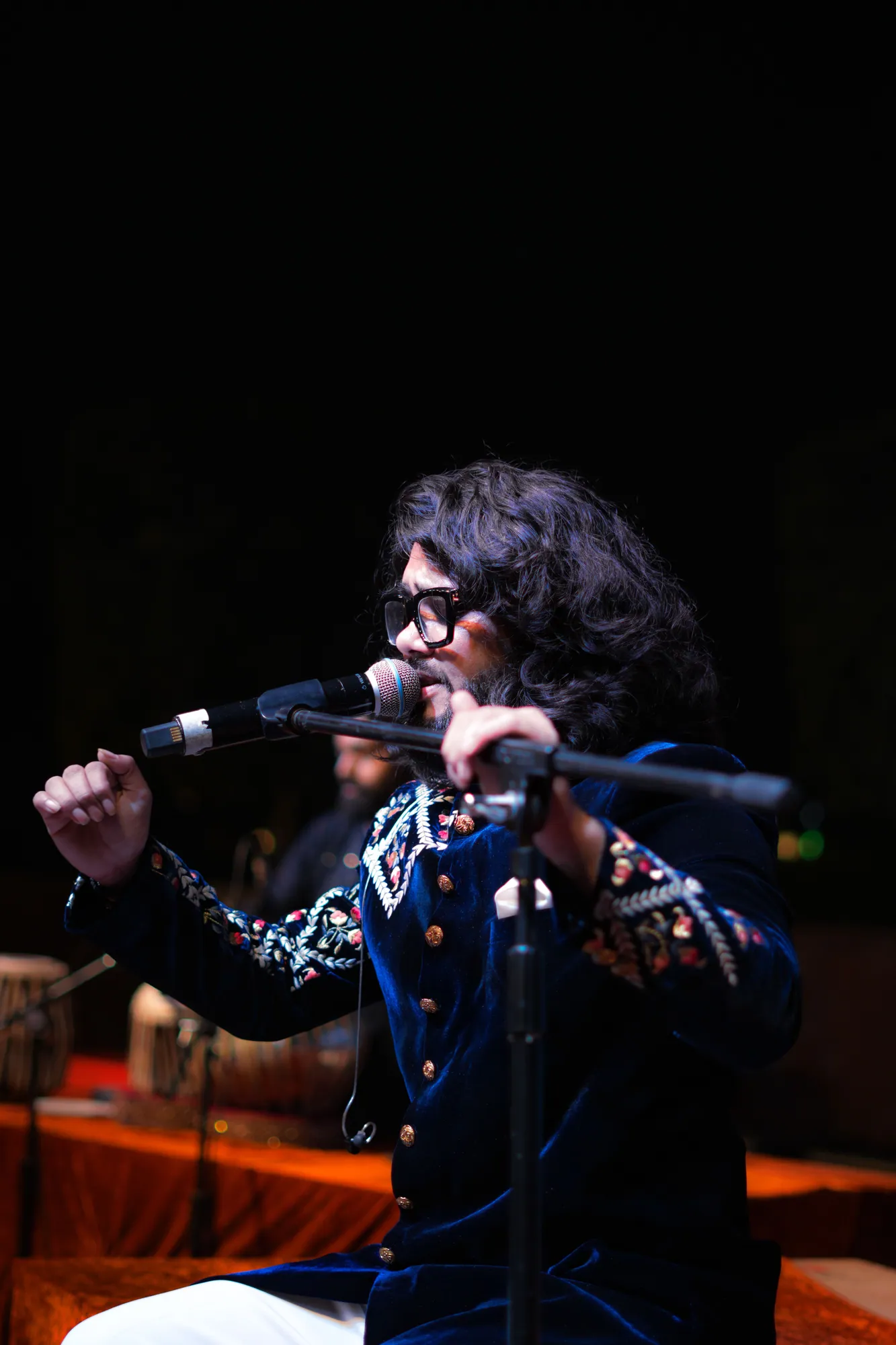 Softrock's vocalist seated, eyes closed and hand raised, singing into the microphone in an embroidered velvet jacket.