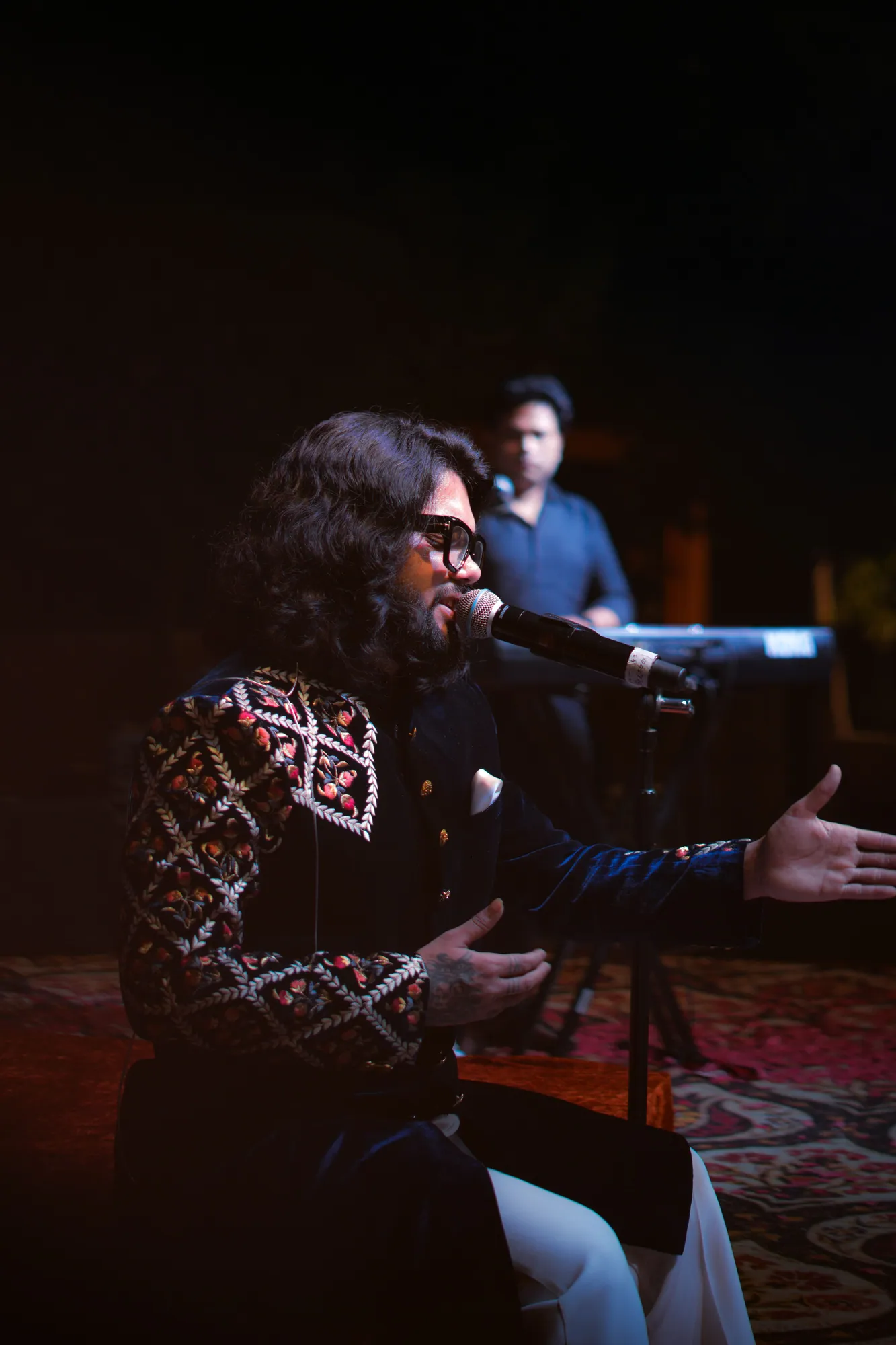 Softrock's vocalist seated and singing with an outstretched hand, the keyboardist behind.