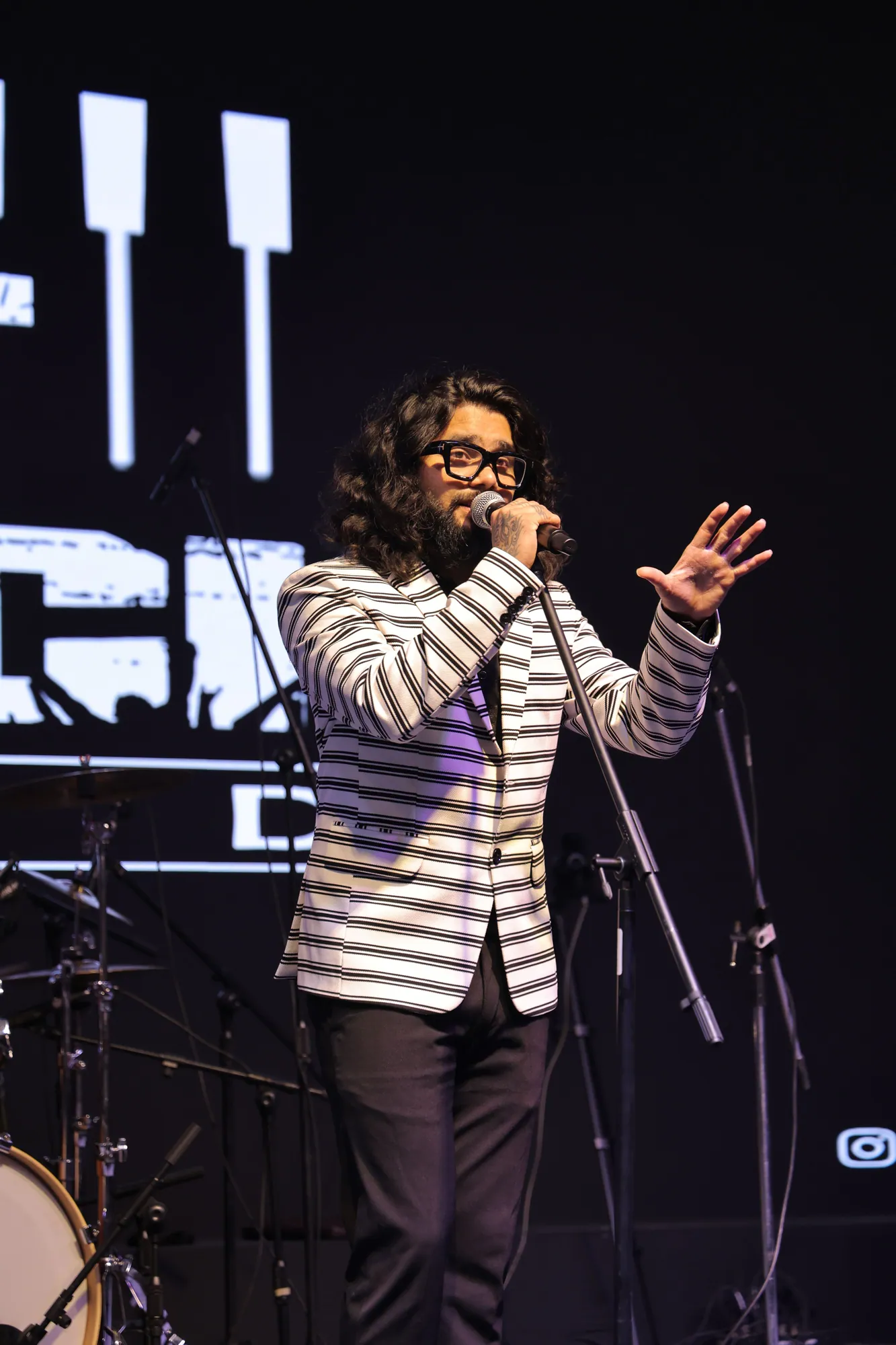 Softrock's vocalist in a striped blazer singing with one hand raised, the drum kit beside.